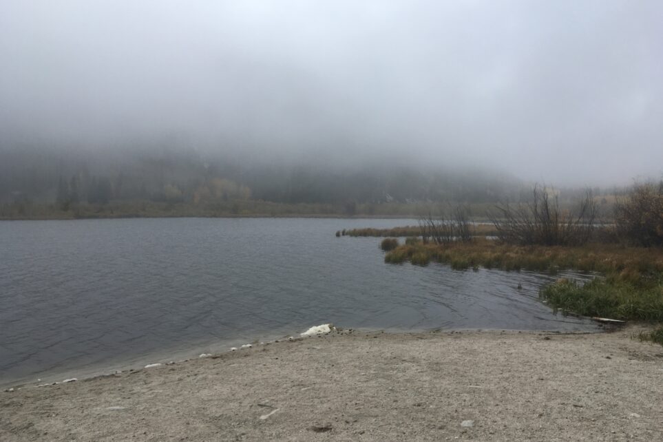 Fog over a quiet lake with the distant shoreline partly hidden