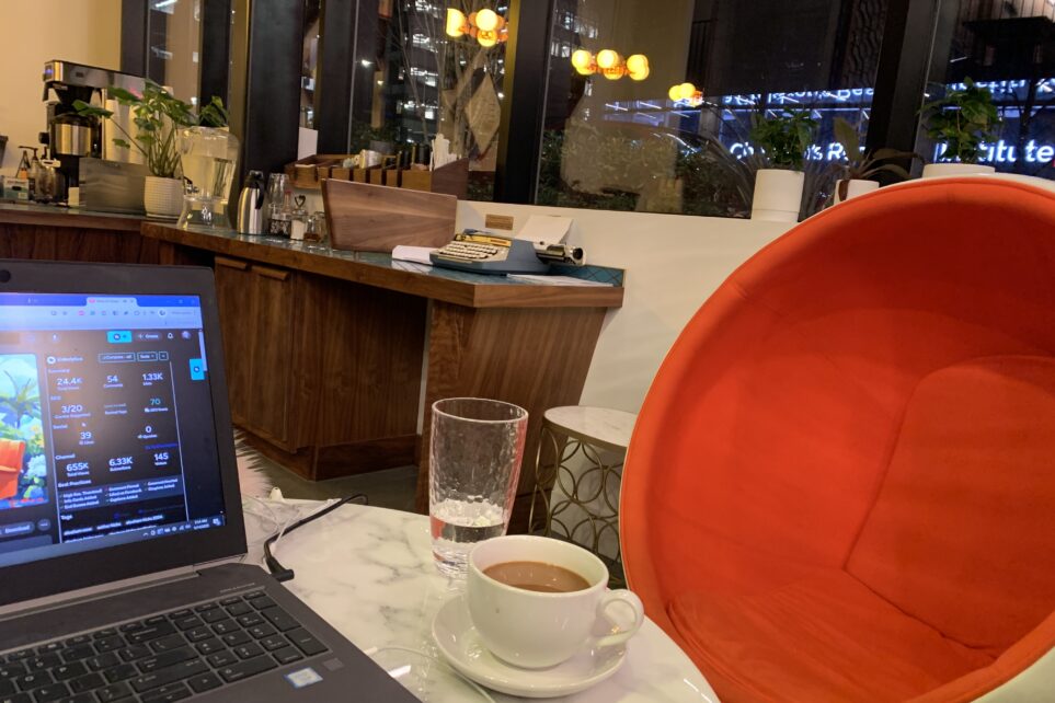 Laptop and coffee on a cafe table beside an empty orange chair